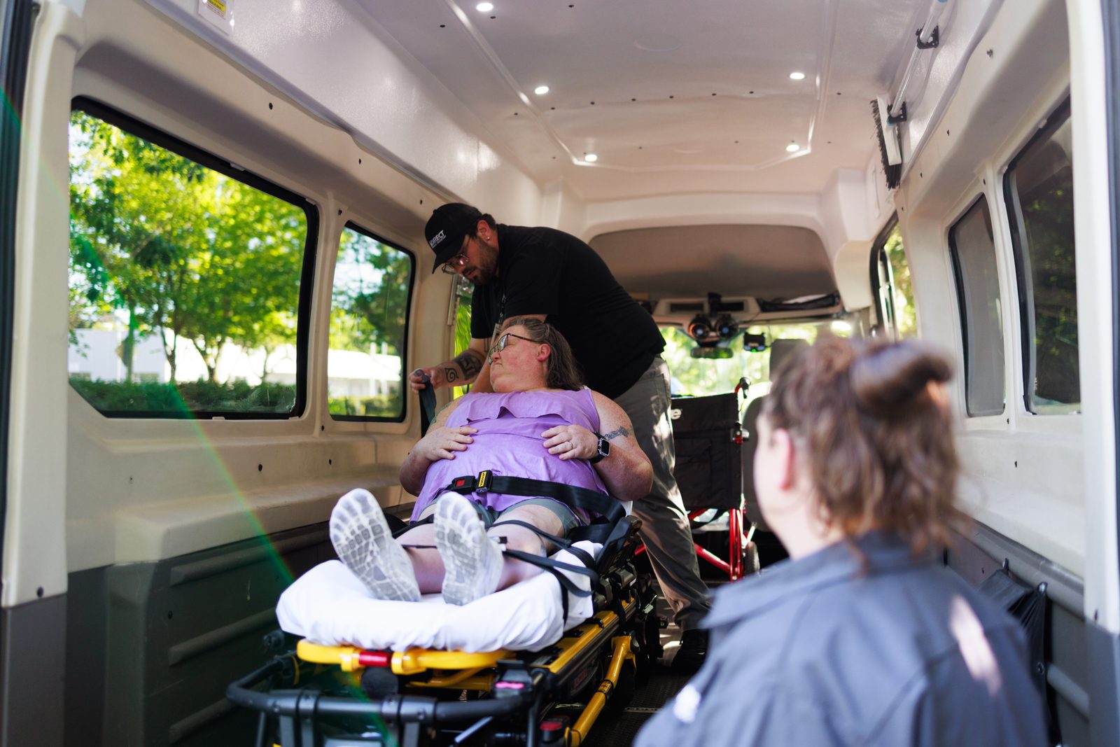 Interior of a Direct Medical Transportation stretcher van with a patient on a gurney and an attendant alongside